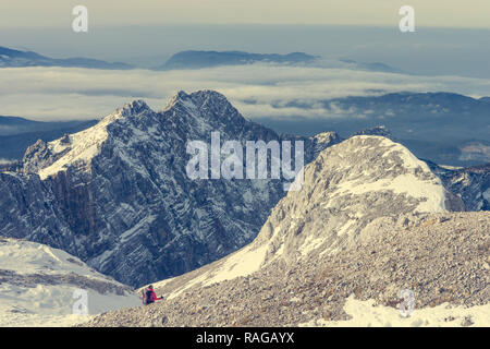 Female alpinist descending into mountain valley crossing flakes of snow. Stock Photo