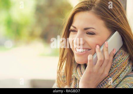 Young brunette outdoors having phone call and smiling in leisure looking away Stock Photo