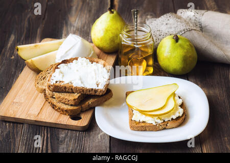 Toast with pear, ricotta cheese and honey on rustic wooden background with ingredients. Healthy breakfast. Stock Photo