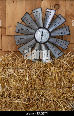 roman numeral tin clock sitting on a bale of hay against an unfinished wood panel wall Stock Photo