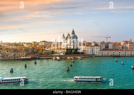 Vaporetto and boats cross the grand canal with the dome of Santa Maria Della Salute Cathedral in the distance as the sun goes down in Venice, Italy Stock Photo
