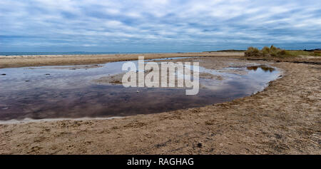 Studland beach on a January day with dramatic cloudy sky and reflection in water. Panoramic landscape. Stock Photo