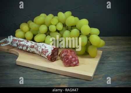 Sliced dry cured Fuet sausage and green grapes on wooden cutting board Stock Photo