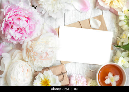 blank greeting card in frame made of peony, rose and jasmine flowers with cup of tea. flat lay. top view Stock Photo