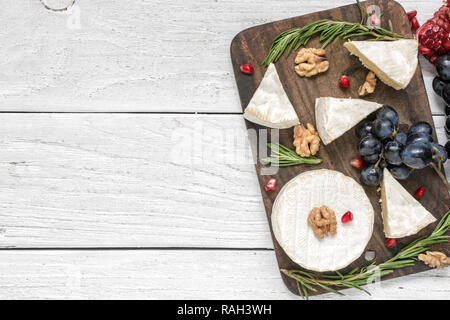 camembert cheese with grapes, pomegranate seeds, walnuts and rosemary on wooden cutting board. top view with copy space Stock Photo