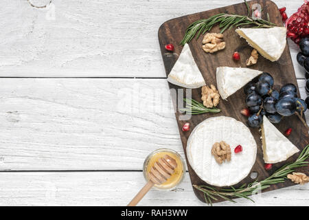 camembert cheese with grapes, honey, pomegranate seeds, walnuts and rosemary on wooden cutting board. top view with copy space Stock Photo