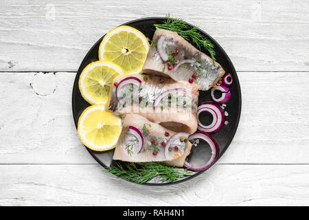 Herring fillet with salt, pepper, herbs, onion and lemon on black plate on white background. top view. healthy food Stock Photo