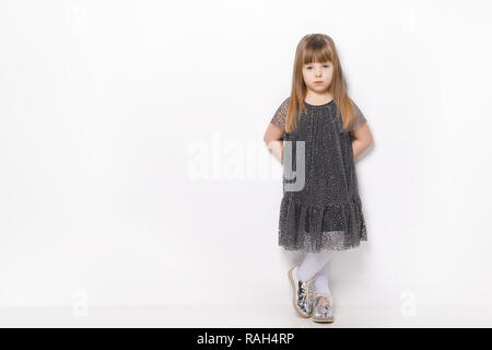 Beautiful little girl with blond hair and blue eyes standing on a white background wearing dress Stock Photo