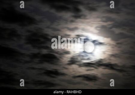 Slightly cloudy night sky, full moon is shining brightly through thin clouds Stock Photo