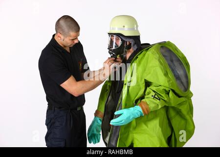 Firefighter helping a colleague put on a chemical protective suit with air supply from a compressed air breathing apparatus, Stock Photo