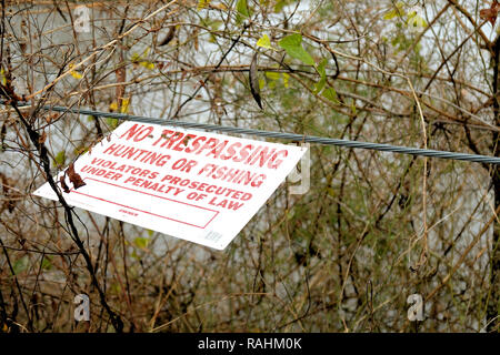 No trespassing, hunting or fishing sign on a steel cable in front of natural foliage. Stock Photo