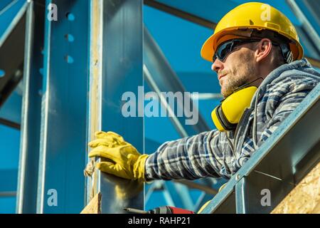Construction Worker Portrait. Caucasian Builder in Yellow Hard Hat and Noise Reduction Headphones. Industrial Theme. Stock Photo