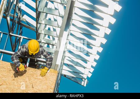 Skeleton Frame Home Construction Worker in Yellow Helmet Installing Metal Elements. Construction Industry Theme. Stock Photo