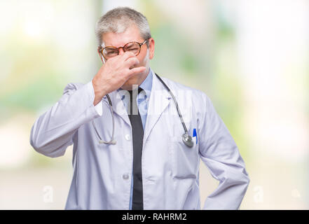 Handsome senior doctor man over isolated background smelling something stinky and disgusting, intolerable smell, holding breath with fingers on nose.  Stock Photo