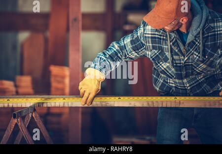 Caucasian Worker in His 30s Measure Wood Beam with Measuring Tape. Stock Photo