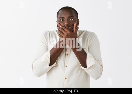 Swear I was not saying word. Portrait of troubled and worried shocked dark-skinned male with short haircut in white shirt, covering mouth with both palms, staring nervous at camera Stock Photo