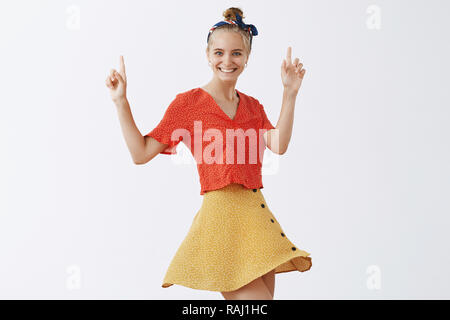 Polka-dot mood turning on. Portrait of cute and feminine european woman wearing vintage clothes and dancing carefree with raised index fingers and joyful smile, having fun over gray background Stock Photo