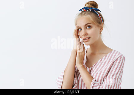Young and beautful. Portrait of tender and gentle good-looking blond woman in striped pink blouse and headband, touching face and gazing at camera with cute relaxed expression Stock Photo