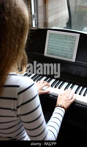 Girl playing the piano, reading the notes from an iPad, tablet computer Stock Photo