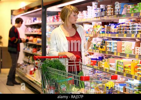 Female customer standing in front of the refrigerated shelf, dairy products, food hall, supermarket