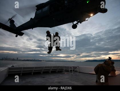 Two members of Coast Guard Maritime Security Response Team West are hoisted back aboard a 129th Rescue Wing helicopter in day- and night-time fast-rope training from the deck of the Hornblower Spirit in San Francisco Bay, December 5, 2018. Team members are trained in advanced techniques with federal partners to protect the nation from a variety of waterborne threats. U.S. Coast Guard photo by Chief Petty Officer John Masson. Stock Photo