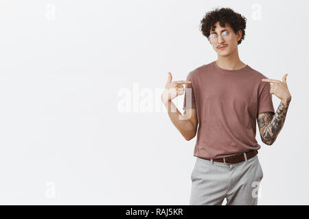 Indoor shot of confident artistic and creative jewish guy with dark curly hair and moustache standing in self-assured pose pointing at himself proudly presenting himself as perfect candidate Stock Photo