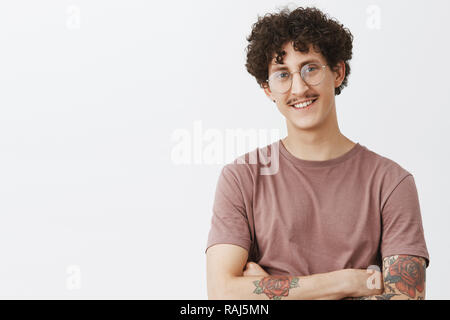 Waist-up shot of stylish and creative confident happy dark-haired guy with curly hair moustache and tattooed arm smiling with self-assured satisfied expression being proud of own achievements Stock Photo
