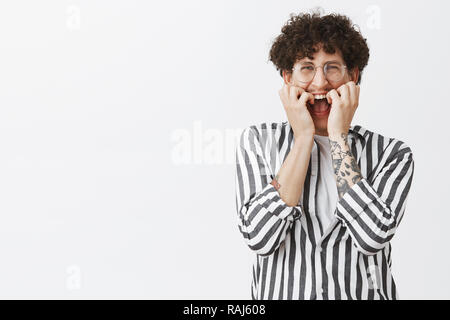 Waist-up shot of timid and insecure funny jewish guy with dark curly hair and moustache in glasses and striped shirt screaming from fear trembling while shouting from fright covering face with hands Stock Photo