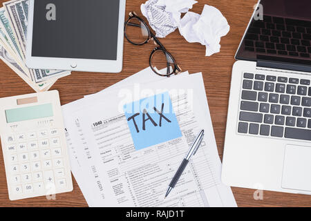 top view of tax forms, digital devices and blue card with 'tax' word on desk Stock Photo
