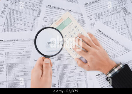 cropped view of man holding magnifying glass and using calculator with tax forms on background Stock Photo
