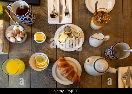A breakfast table with a croissant, preserves and orange juice. Teacups also stand on the table. Stock Photo