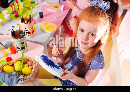 children in kindergarten paint eggs for the Easter basket at the table.  Stock Photo