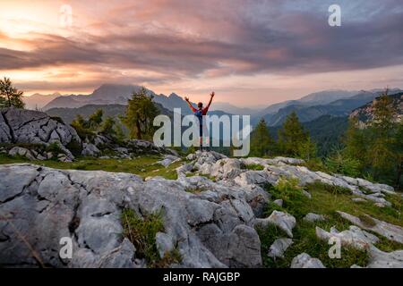 Hiker stretches his arms into the air, summit of Feldkogel, view of Königssee at sunset, left Watzmann Südspitze and Stock Photo