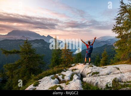 Hiker stretches his arms into the air, summit of Feldkogel, view of Königssee at sunset, left Watzmann Südspitze and Stock Photo