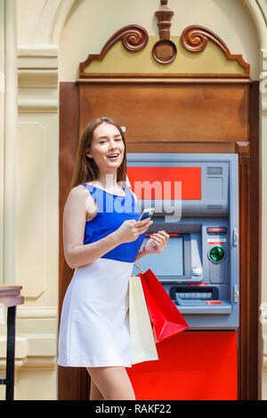 Young happy brunette woman withdrawing money from credit card at ATM Stock Photo