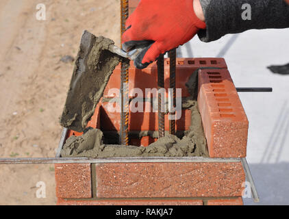 Bricklayer hand laying brick column with metal rod Stock Photo