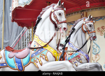 Beautiful white horses Christmas carousel in a holiday park. Two horses on a traditional fairground vintage Paris carousel. Merry-go-round with horses Stock Photo