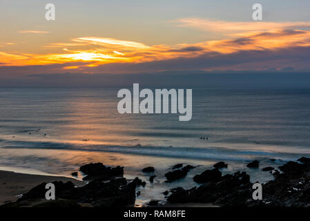 Long exposure sunset over surfers on Fistral Beach, Newquay, Cornwall, UK Stock Photo