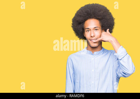 Young african american man with afro hair smiling doing phone gesture with hand and fingers like talking on the telephone. Communicating concepts. Stock Photo