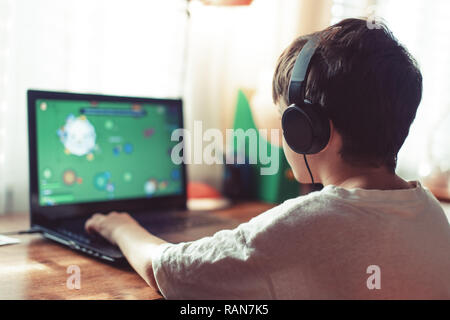 Little dependent gamer boy playing on laptop indoors Stock Photo