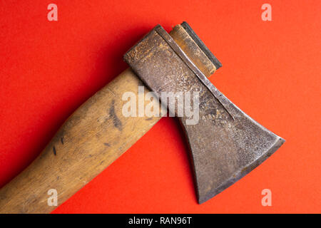 The old ax lies on the ground. Old ax with wooden handle on a bright red orange purple background top view. Stock Photo