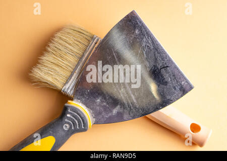 Metal spatula, trowel with plastic handle and two paint brush on white background with copyspase. Brush and spatula - paint tools on a beige and brigh Stock Photo