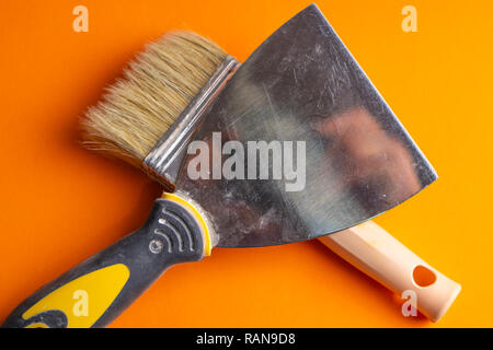 Metal spatula, trowel with plastic handle and two paint brush on white background with copyspase. Brush and spatula - paint tools on a beige and brigh Stock Photo