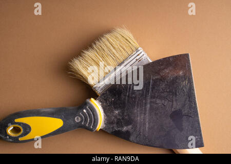 Metal spatula, trowel with plastic handle and two paint brush on white background with copyspase. Brush and spatula - paint tools on a beige and brigh Stock Photo
