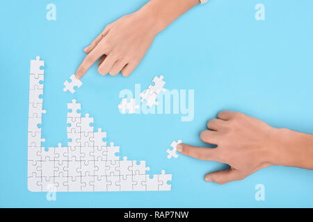 cropped shot of man and woman with white puzzle pieces on blue backdrop, cooperation concept Stock Photo