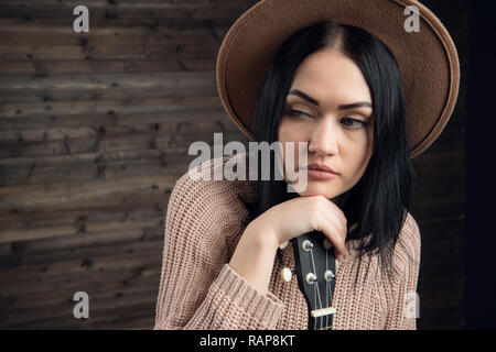 Close up portrait of young caucasian woman playing ukulele in front of a wooden background. Studio shot, leisure activities concept. Stock Photo