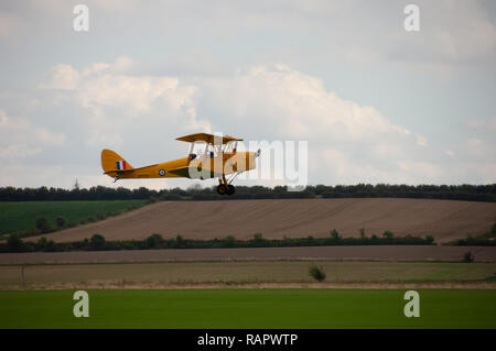 A yellow biplane flies over Duxford Imparial War Museum Stock Photo