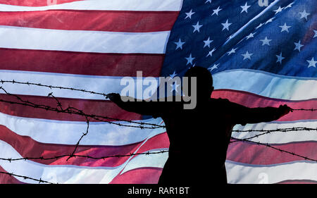 Man looking through barbed wire/razor wire fence with USA stars and stripes flag in background. Immigration, border fence, Mexican border... concept Stock Photo