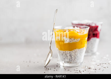 Tasty healthy appetizing yogurt desserts with chia seeds, mango and berry puree in glasses. Closeup with copy space. Grey Background. Stock Photo