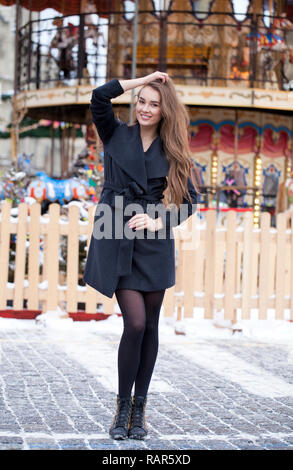 Portrait in full growth of a beautiful young brown haired woman on the background of a winter amusement park Stock Photo